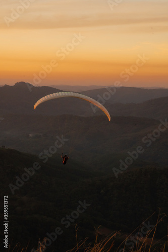 Paragliding concept, Beauty nature mountain landscape. Paraglider silhouette flying over misty mountain valley in beautiful warm sunset.