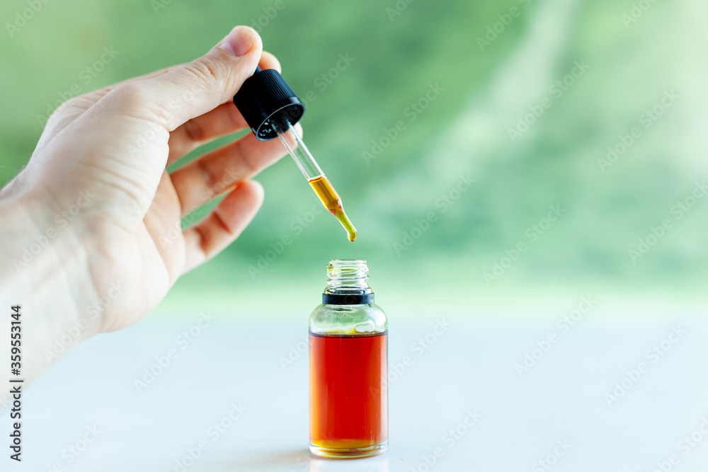close-up hand holds a dropper over a jar of oil close-up hand holds a dropper over a jar of oil