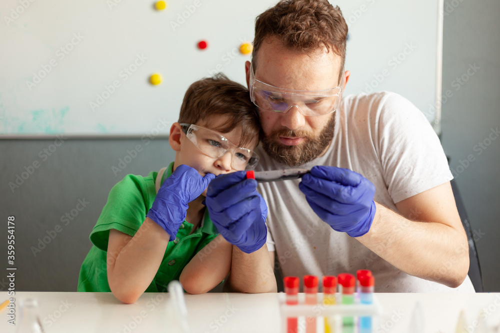 a man and a boy carefully examine a test tube with dark liquid, sit at a table in a laboratory a man and a boy carefully examine a test tube with dark liquid, sit at a table in a laboratory