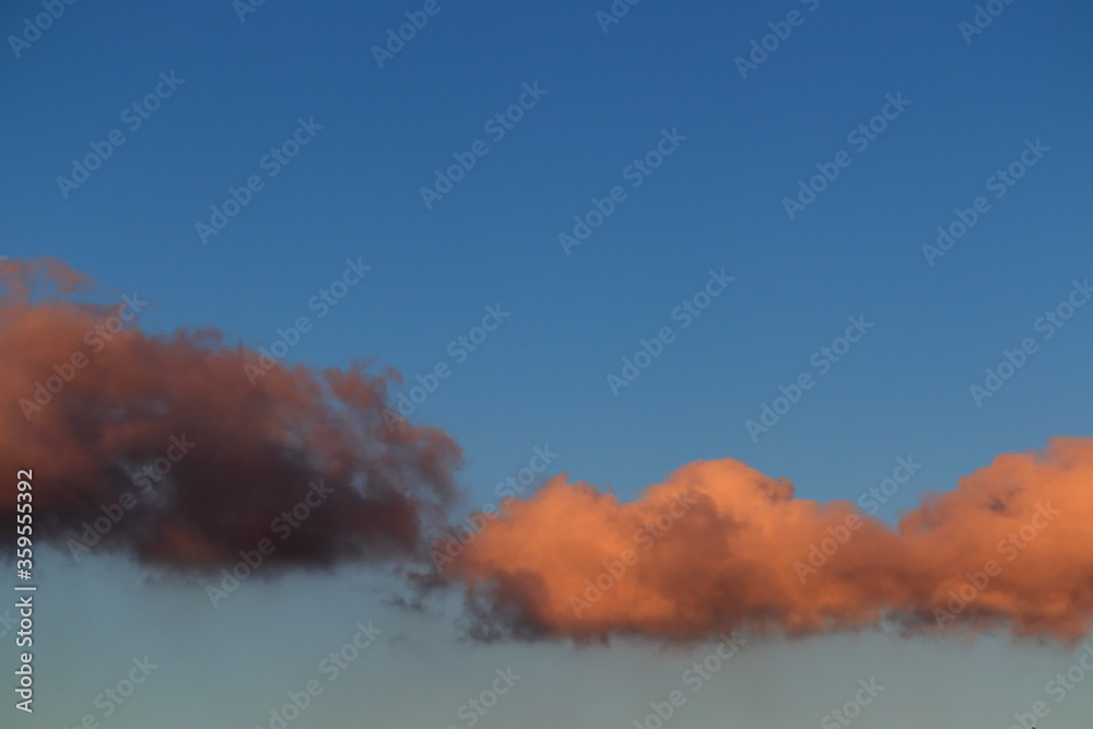 a cloud shaded with brown and another shaded with orange, floating together under a blue sky.
