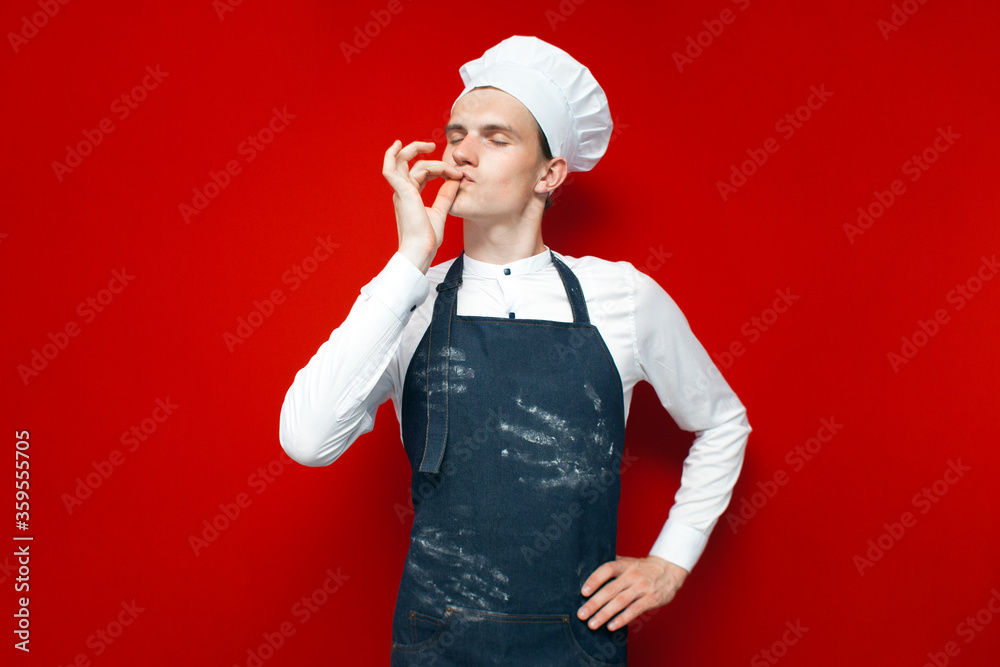 cook shows gesture of good taste on a red isolated background, guy in the form of a chef makes a hand sign cook shows gesture of good taste on a red isolated background, guy in the form of a chef makes a hand sign