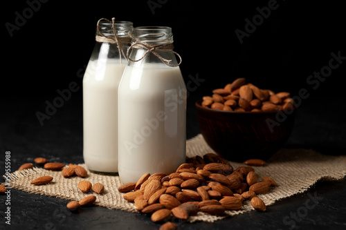 two bottles of almond milk with nuts on a dark black table  vegetarian milk without sugar and lactose