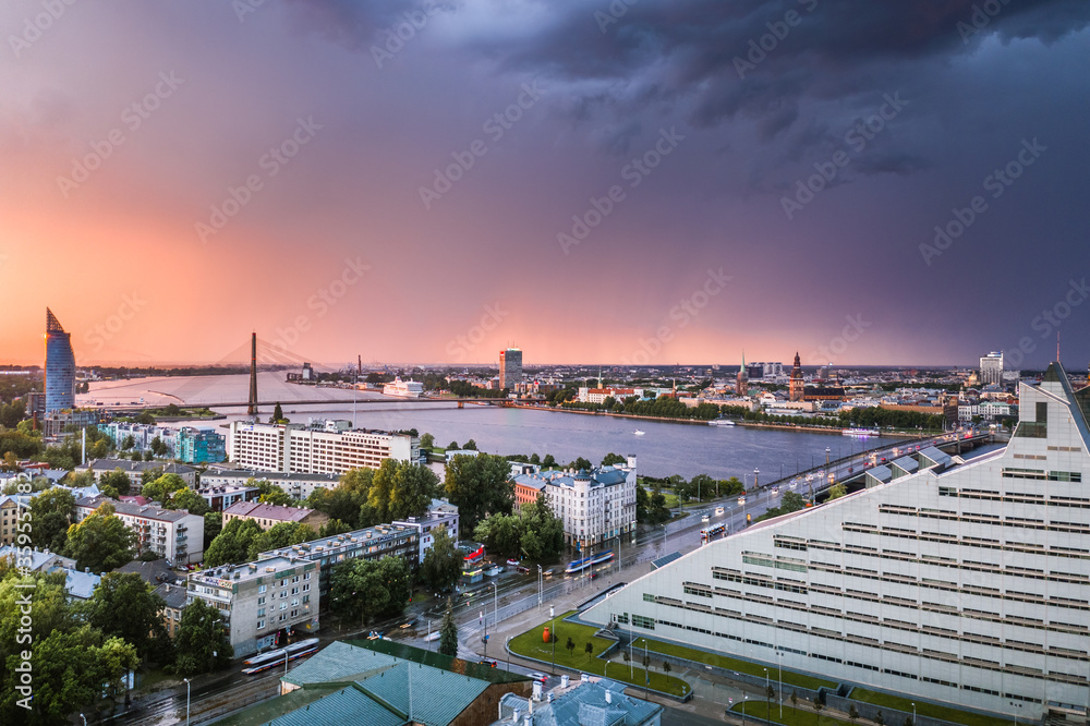 Aerial view of iconic Riga city downtown in dramatic sunset. Modern architecture in rainy weather with storm clouds in warm colors. 