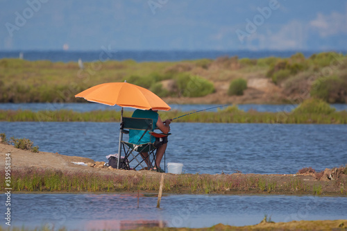 hombre de vacaciones pescando debajo de su sombrilla naranja