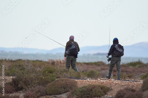 dos hombres con sus cañas de pescar y sus mochilas anda hacia el mar