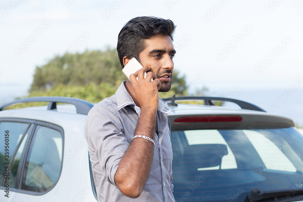 Man talking on a cell phone leaning on the door of his car