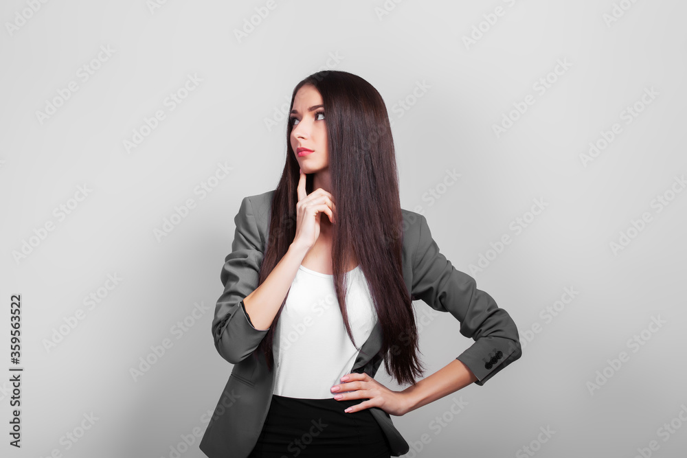 Beautiful business woman with dark hair, thinking standing on a gray background Beautiful business woman with dark hair, thinking standing on a gray background