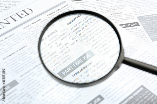 Looking through magnifying glass at newspaper  closeup. Job search concept