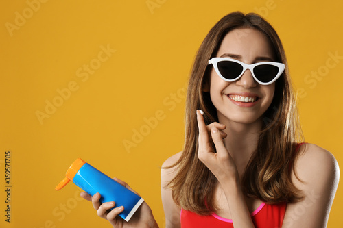 Young woman applying sun protection cream on orange background. Space for text