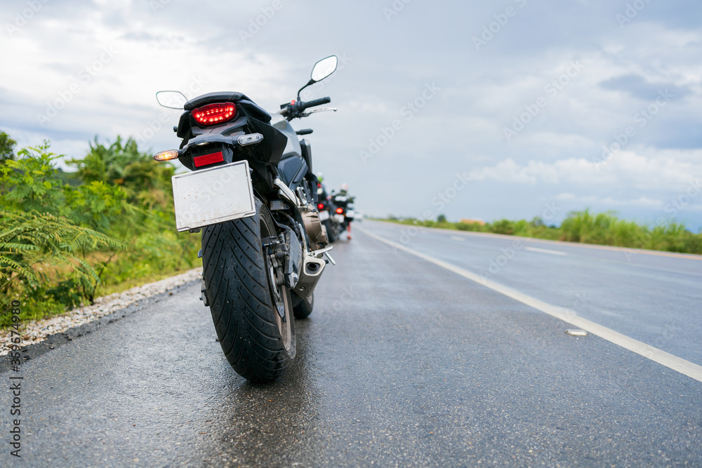 Obraz premium zbliżenie motocykl motoroweru jeździ przez kałużę na mokrej drodze w deszczu z nieostrością i nad światłem w tle