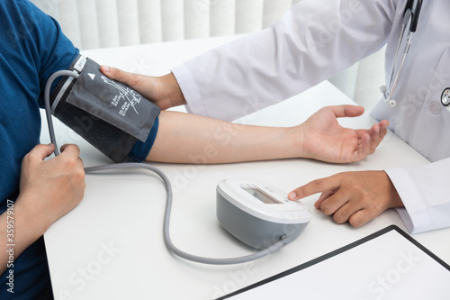 The doctor is measuring blood pressure on the patient arm with the blood pressure monitor in the hospital.