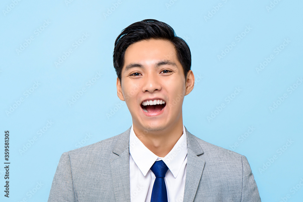Close up portrait of happy young Asian businessman laughing isolated studio blue background Close up portrait of happy young Asian businessman laughing isolated studio blue background