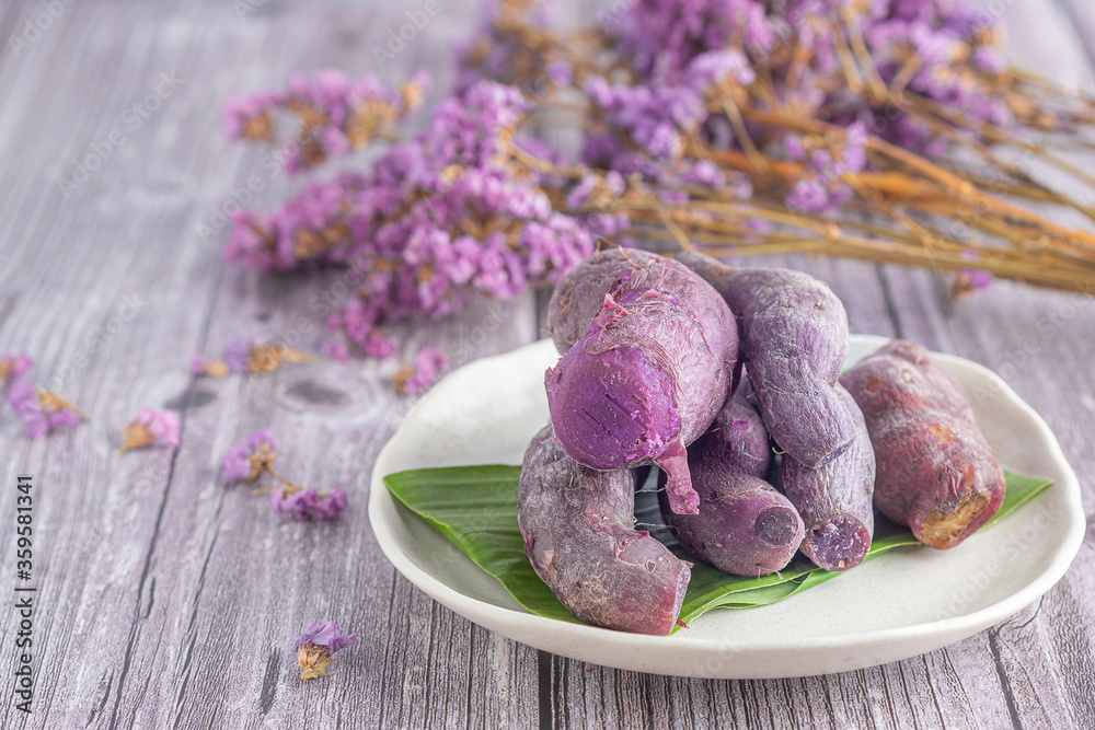 Pile of ripe purple yams is placed on a plate on a wooden table