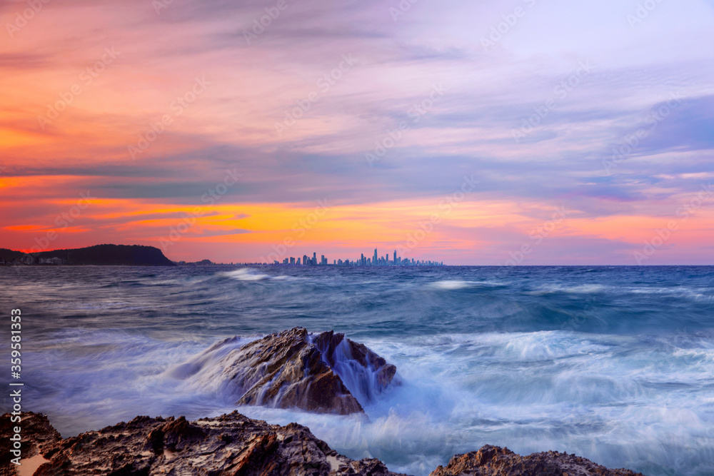 Colourful sunset view of Gold Coast cityscape, with ocean water cascading down rocks Currumbin Rock