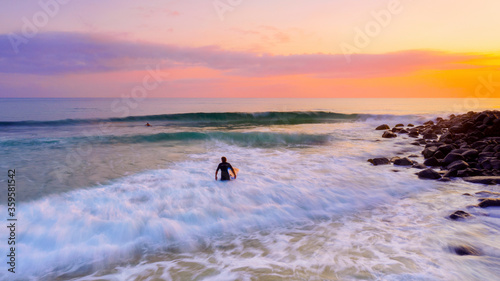 Surfer wading into the ocean with sunrise glow. Burleigh Heads  Gold Coast