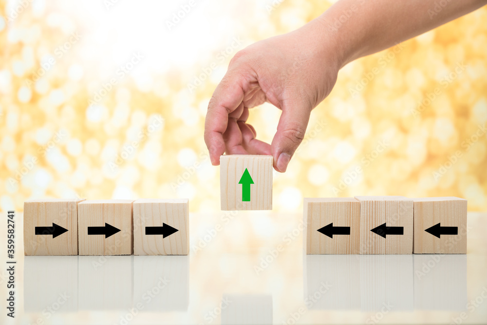 man hand pick up green arrow wood cube from rows of black arrow wood cube