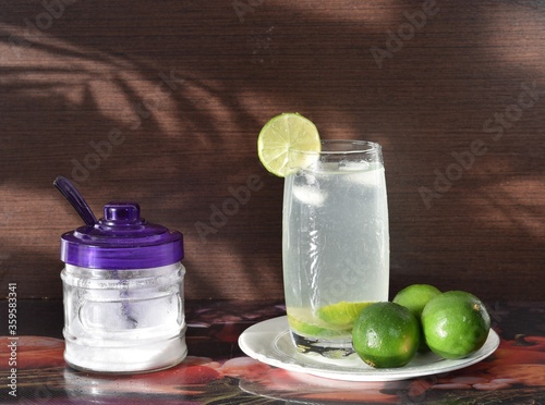 Vaso de refrescante limonada acompañada de hielo, limones y una jarra de azúcar, lista para consumir por la tarde.