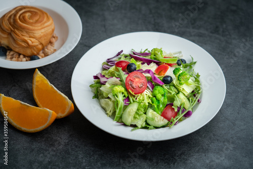 A plate of healthy salad and a breakfast bread.A plate of delicious and healthy vegetable salad on a gray concrete floor.