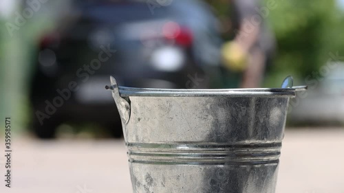 A man washes a car on the street, then throws a sponge into a distant bucket with splash of detergent, slow motion. A domestic hand washing car with soapy water. photo