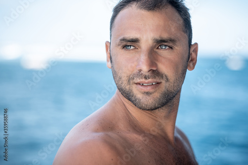 Portrait of handsome man with white teeths, blue eyes, surfer and blue ocean on background
