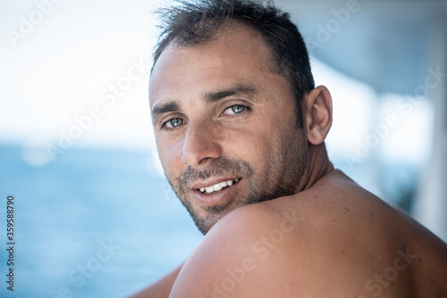 Portrait of handsome man with white teeths smile, blue eyes, surfer and blue ocean on background