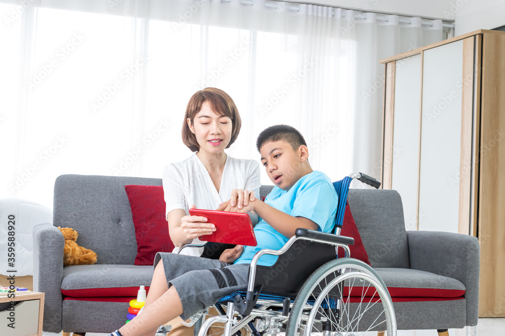 asian woman playing with disabled child on wheelchair by tablet in living room. asian woman playing with disabled child on wheelchair by tablet in living room.