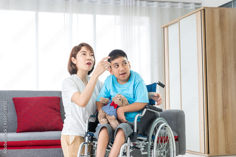asian woman taking care disabled child on wheelchair in living room. both looking at something. asian woman taking care disabled child on wheelchair in living room. both looking at something.