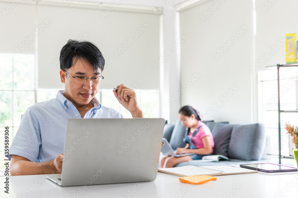 father presenting with laptop on desk and daughter sitting on sofa in living room. work from home concept father presenting with laptop on desk and daughter sitting on sofa in living room. work from home concept