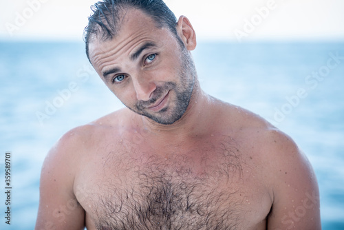 Portrait of handsome man with  blue eyes, shirtless surfer and blue ocean on background on background © Lila Koan