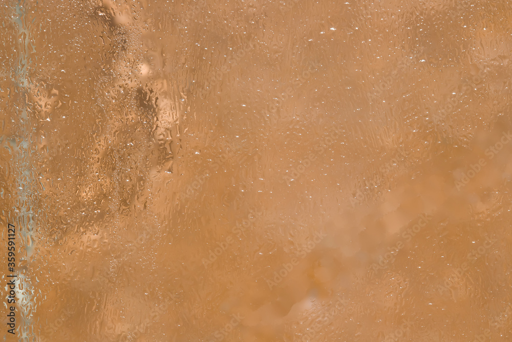 Fototapeta premium Texture. A fragment of a glass surface covered with a thin layer of melting ice is located on a light brown background. Close-up.
