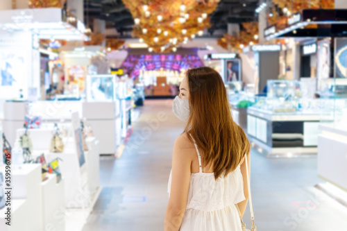 Beautiful young Asian woman in white dress with face mask walking at shopping center or department store, blur background, Shopping, new normal lifestyle concept
