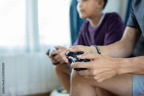 Asian father and son enjoy playing video games together with video joystick with excite and very fun in the living room at home