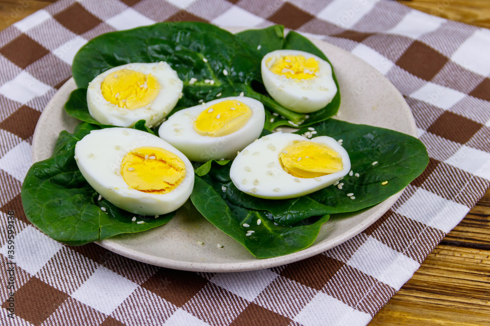 Boiled eggs with fresh spinach leaves and sesame seeds on wooden table Boiled eggs with fresh spinach leaves and sesame seeds on wooden table