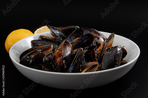 Protein and zinc rich sea food, marine delicacy and luxury foods concept with photograph of a bowl of raw mussels and lemons isolated on black background with clipping path cutout