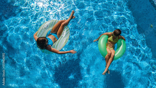 Active children in swimming pool aerial top view from above, happy kids swim on inflatable ring donuts and have fun in water on family holiday vacation on resort 