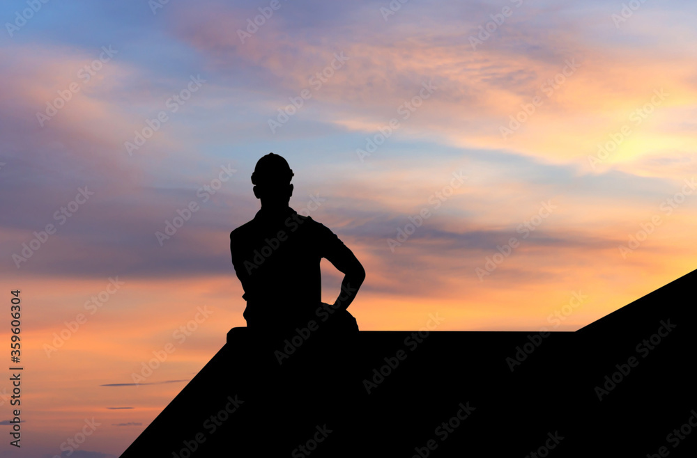 Silhouette of Foreman in hard hat sitting on container box with sunset sky