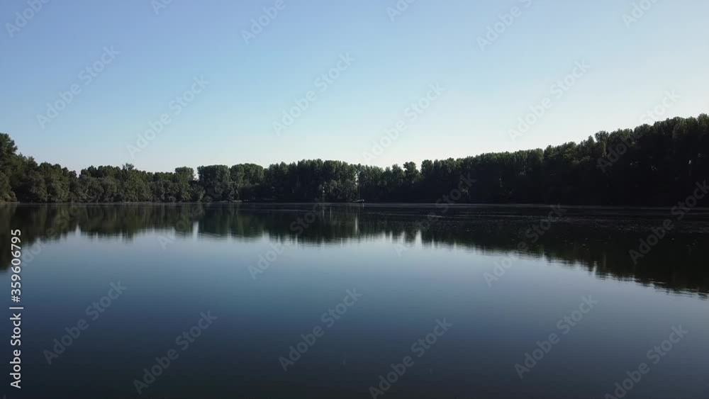 Drone flying close over the water of a dark eerie lake with reflections of trees and blue skies in Europe Drone flying close over the water of a dark eerie lake with reflections of trees and blue skies in Europe