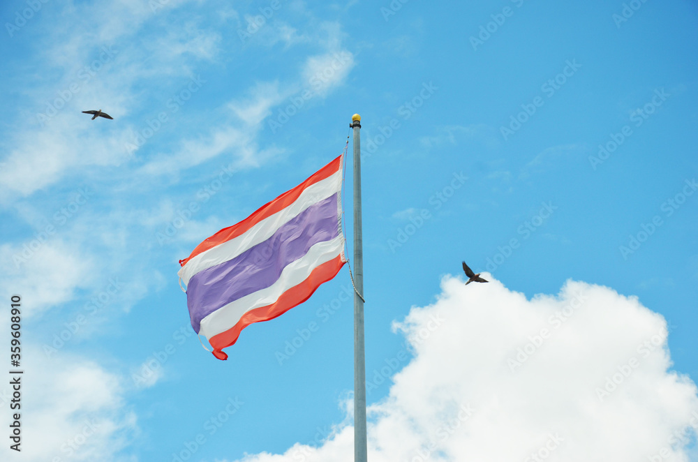 The flag of Thailand is atop a pole with a background in the sky.