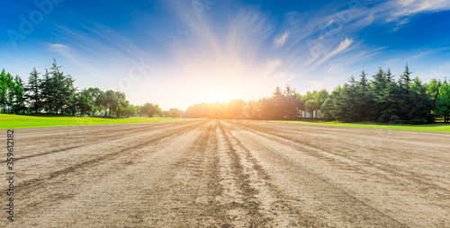 Rural dirt road ground and green forest at sunrise.