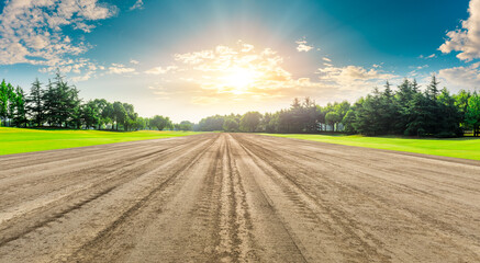 Rural dirt road ground and green forest at sunrise.