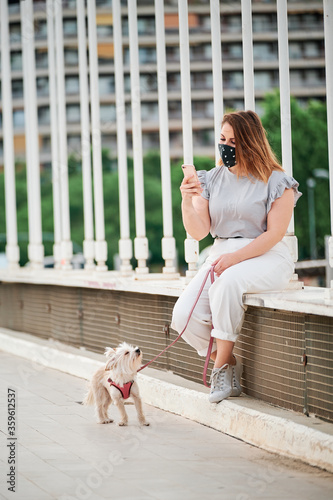 a curvy model using her mobile phone with her dog in an urban scene