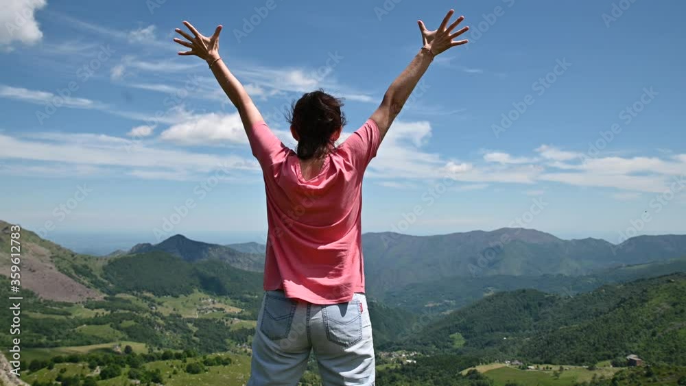 A Caucasian woman with her back is inspired by nature: the landscape of the green valley of the mountain is enchanting. Slowly raise your arms to the sky. A Caucasian woman with her back is inspired by nature: the landscape of the green valley of the mountain is enchanting. Slowly raise your arms to the sky.