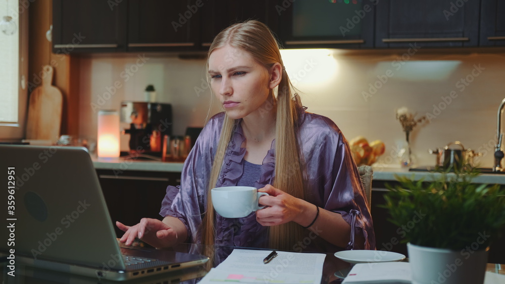 Working at home: Busy business woman in home bathrobe drinking a cup of coffee. She sitting at the computer in the kitchen. Working at home: Busy business woman in home bathrobe drinking a cup of coffee. She sitting at the computer in the kitchen.