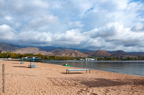Beautiful sand beach of Issyk-Kul lake near Cholpon-Ata city with view over Ruh Ordo cultural complex with dramatic grey heavy clouds, Kyrgyzstan landscape