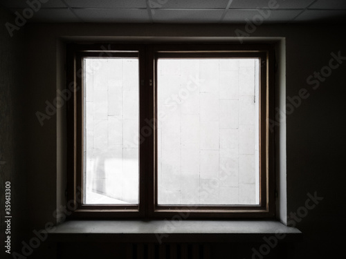 Window overlooking the wall. Silhouette of a window in dark interrior behind which the wall is visible. Textured silhouette of window.