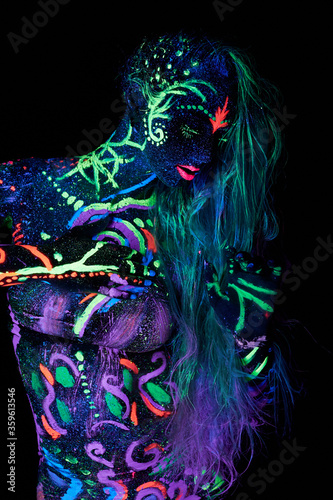 Art woman body art on the body dancing in ultraviolet light. Bright abstract drawings on the girl body neon color. Fashion and art woman, out of focus