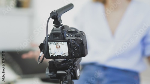 Video camera with microphone on the top is recording video of female blogger