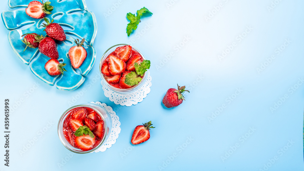 Sweet dessert in glass with berry fruit strawberries and whipped cream on a blue background. Long banner format, top view
