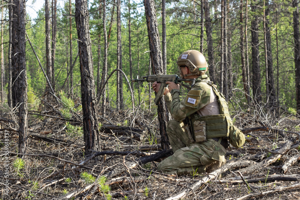 Fully armed american soldier takes aim for a shot in the summer forest, active military game airsoft.