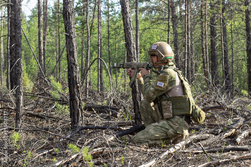 Fully armed american soldier takes aim for a shot in the summer forest  active military game airsoft.